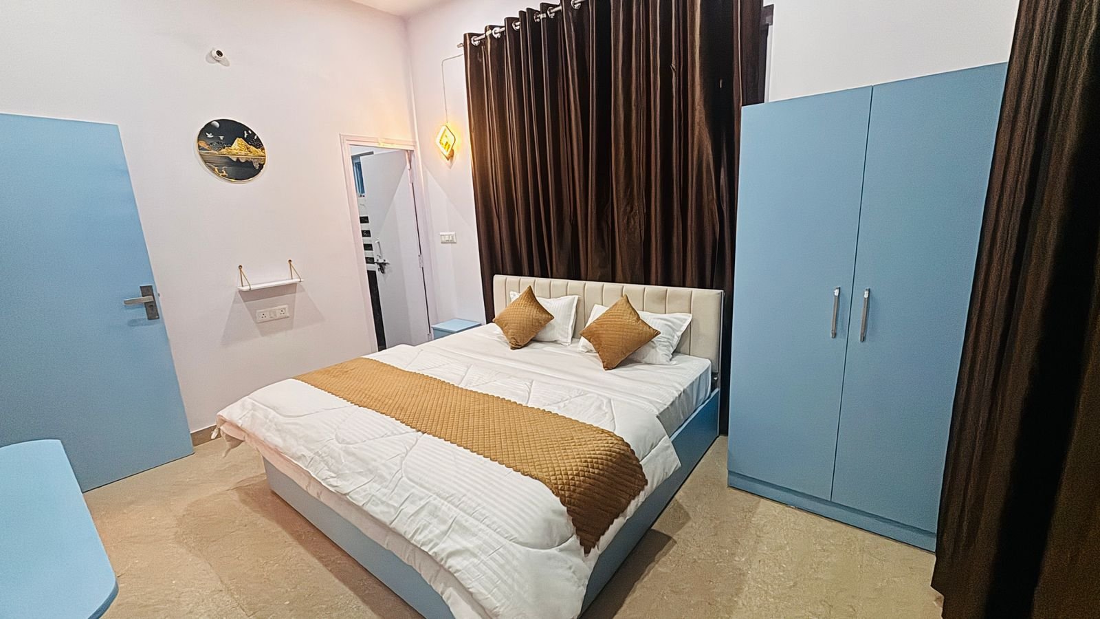 Standard guest room with white linens, mustard pillows, light blue wardrobe, and mountain art on the wall